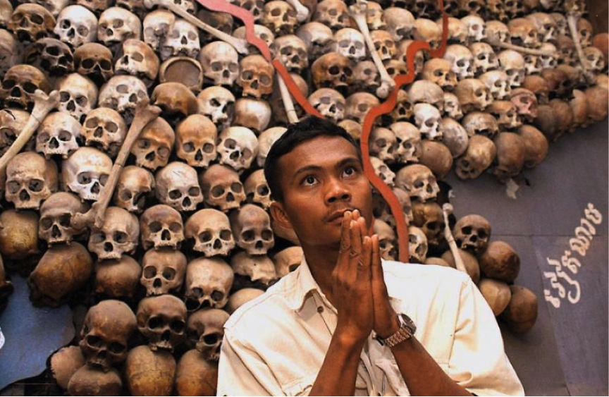 “A Cambodian looking skyward in front of skulls placed in the shape of Cambodia. LF wonders if his prayers relate to what the yanks did that killed millions and then assured the rise of the Khmer Rouge”